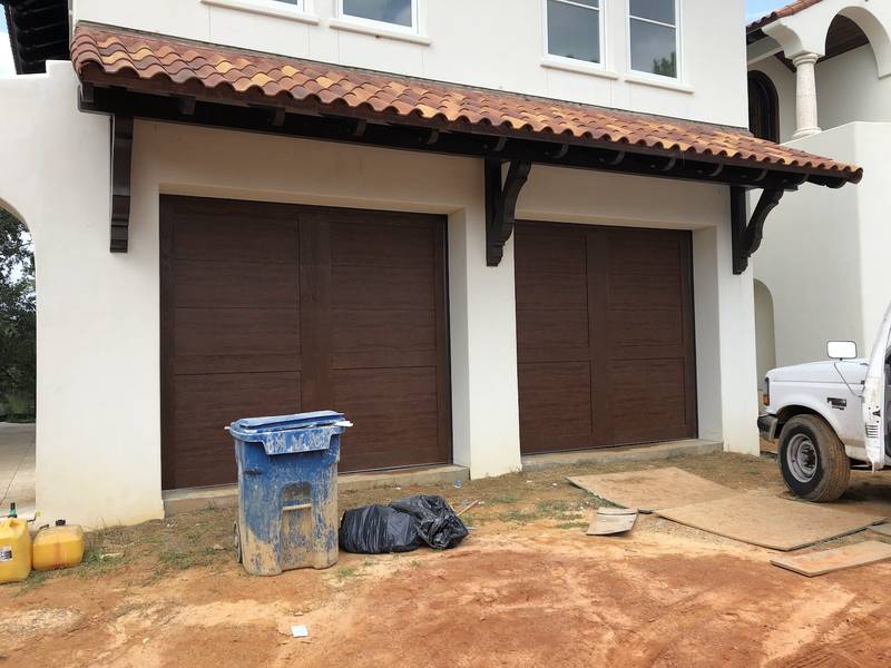 Two brown wood-look garage doors on a stucco house.