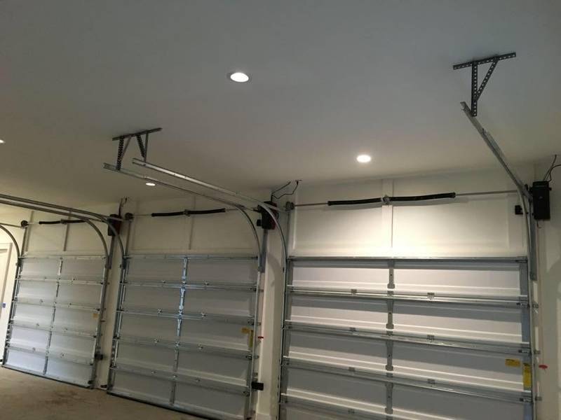 Inside a garage: three sectional doors with torsion springs, opener rails and an opener motor.