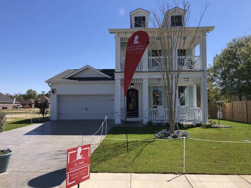 A white house with St. Jude Dream Home signs out front and a white garage door.