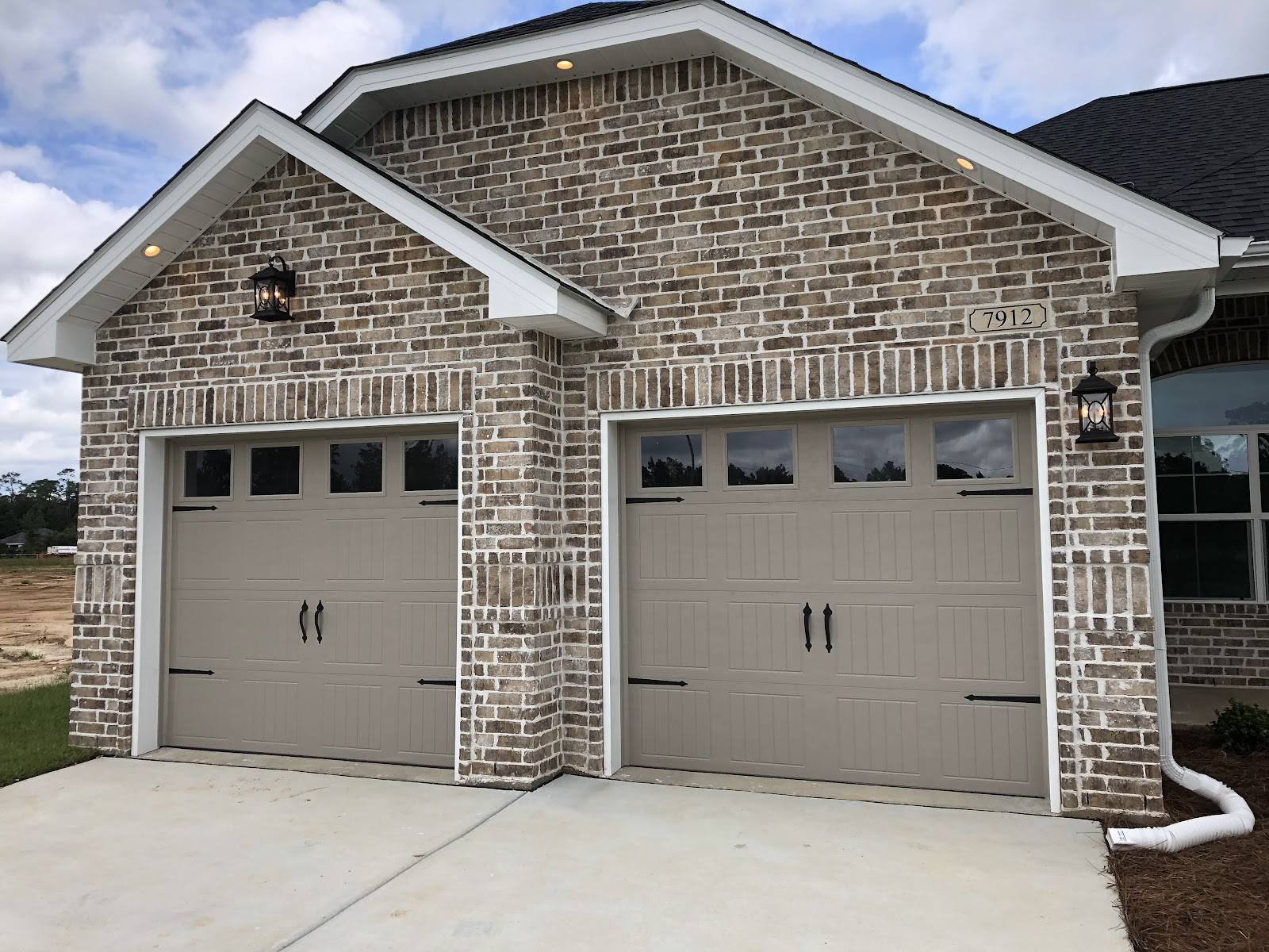 Two tan carriage-style garage doors with window tops on a brick house, installed by J M Doors.